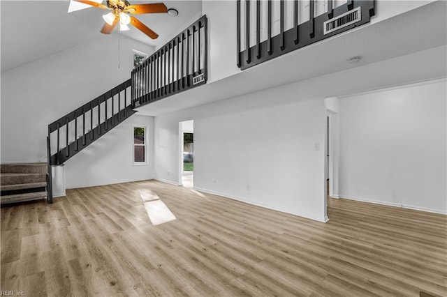 unfurnished living room featuring ceiling fan, a towering ceiling, light hardwood / wood-style flooring, and a wealth of natural light