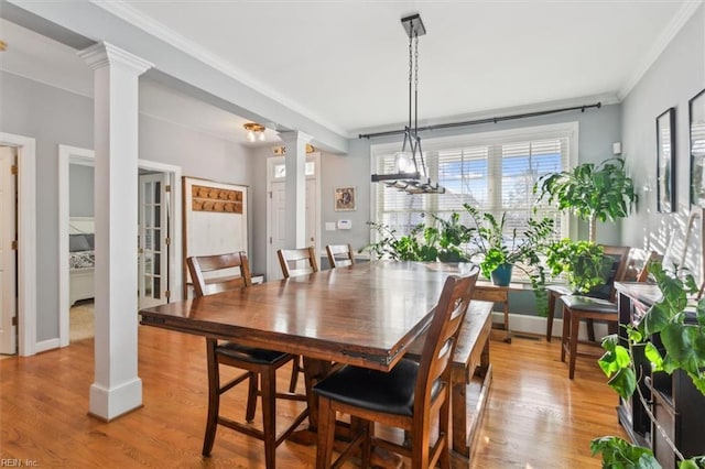 dining space with decorative columns, crown molding, and light wood-type flooring