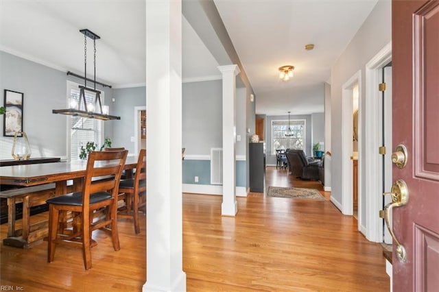 dining space with a notable chandelier, ornamental molding, light wood-type flooring, and ornate columns