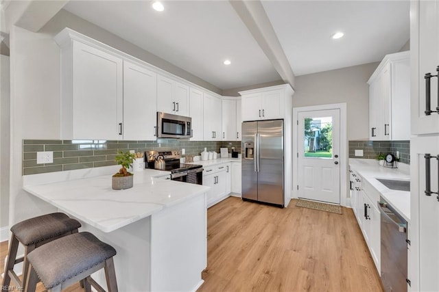 kitchen featuring tasteful backsplash, white cabinetry, a breakfast bar area, light hardwood / wood-style floors, and stainless steel appliances