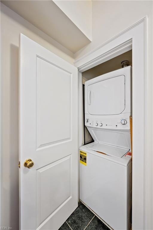 laundry area with stacked washer and dryer and dark tile patterned flooring