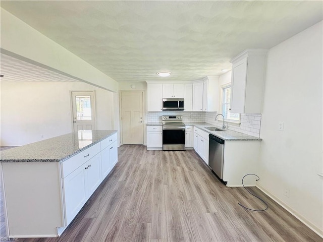 kitchen with appliances with stainless steel finishes, sink, white cabinets, decorative backsplash, and light stone countertops