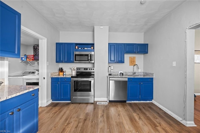 kitchen featuring dark wood-type flooring, stainless steel appliances, washing machine and dryer, and blue cabinets