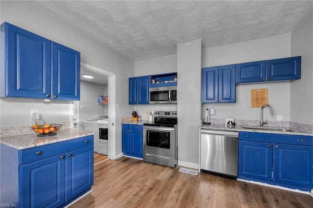 kitchen with appliances with stainless steel finishes, blue cabinets, sink, and light stone countertops