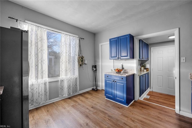 kitchen featuring black fridge, blue cabinetry, and light hardwood / wood-style flooring