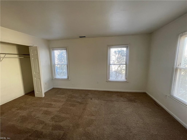 unfurnished bedroom with multiple windows, dark carpet, and a closet