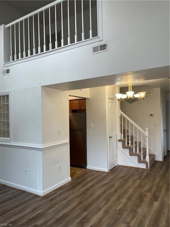 unfurnished living room featuring a notable chandelier, dark wood-type flooring, and a high ceiling