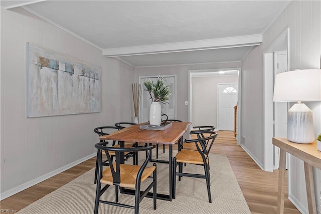 dining space featuring ornamental molding, beam ceiling, and light hardwood / wood-style flooring