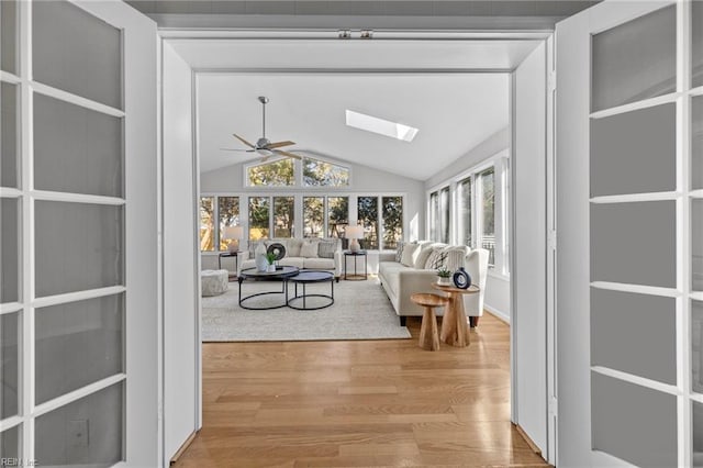 living room featuring ceiling fan, plenty of natural light, lofted ceiling with skylight, and light wood-type flooring