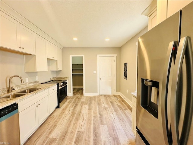 kitchen with light stone counters, white cabinetry, appliances with stainless steel finishes, and sink