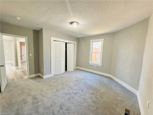 unfurnished bedroom featuring light carpet, a textured ceiling, and a closet