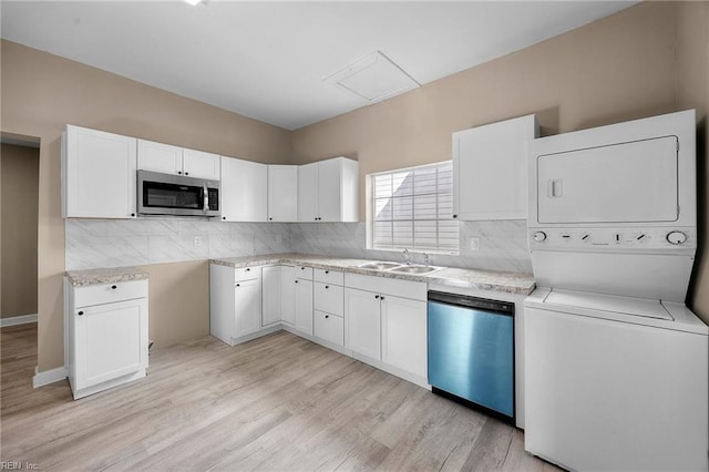 kitchen with sink, stainless steel appliances, stacked washer / drying machine, light hardwood / wood-style floors, and white cabinets