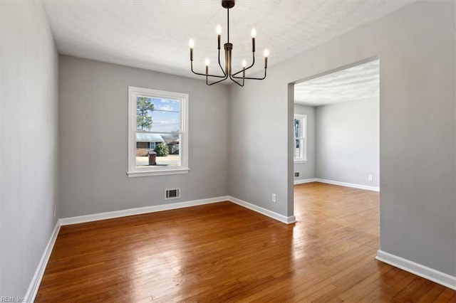 spare room with hardwood / wood-style flooring and an inviting chandelier