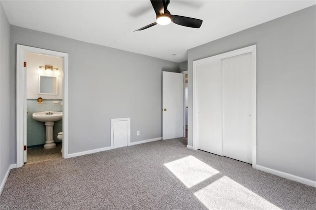 unfurnished bedroom with ensuite bath, a closet, ceiling fan, and carpet flooring