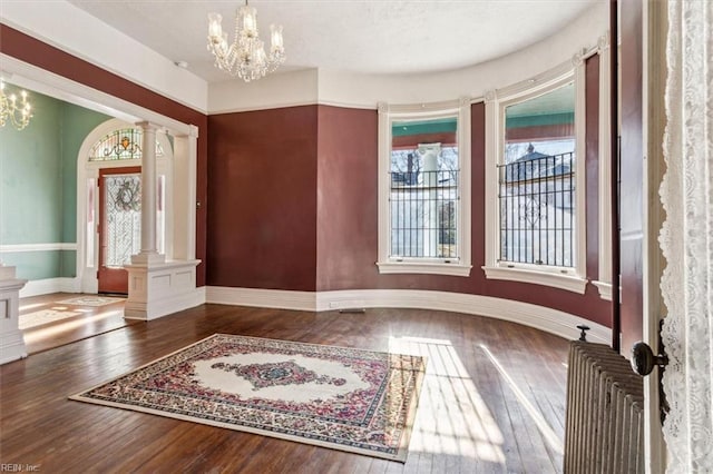 interior space featuring ornate columns, dark wood-type flooring, and a chandelier