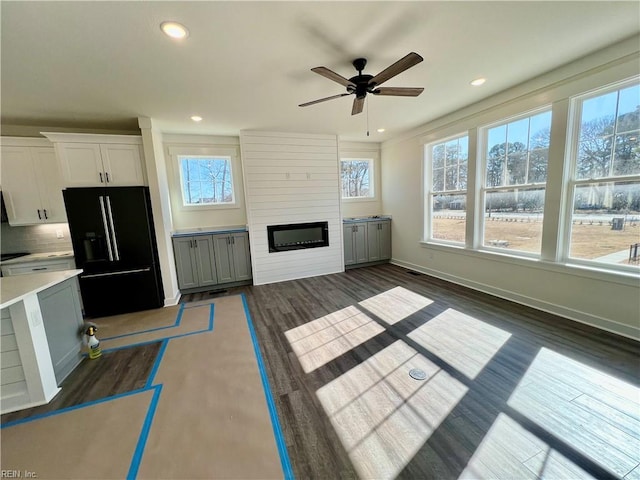 unfurnished living room featuring dark wood-type flooring, a large fireplace, and ceiling fan