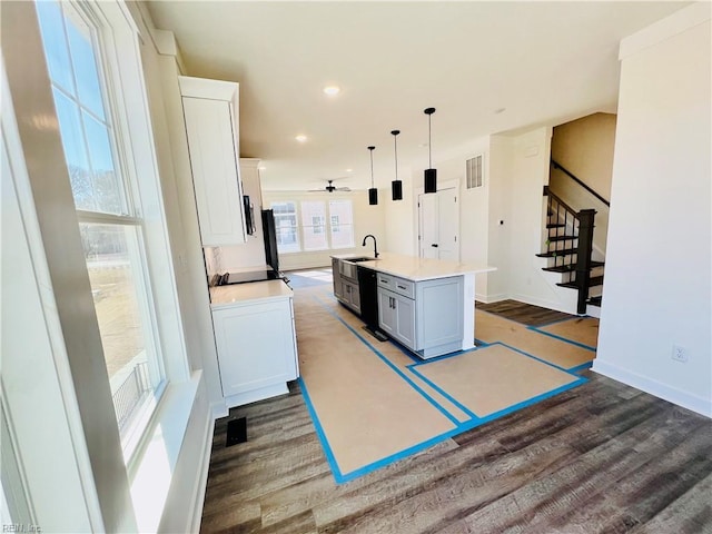 kitchen featuring sink, dishwasher, hanging light fixtures, white cabinets, and a center island with sink