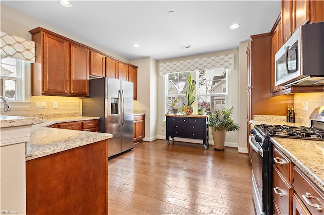 kitchen featuring stainless steel appliances, tasteful backsplash, light stone countertops, and dark hardwood / wood-style floors