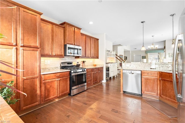 kitchen featuring tasteful backsplash, wood-type flooring, appliances with stainless steel finishes, and decorative light fixtures