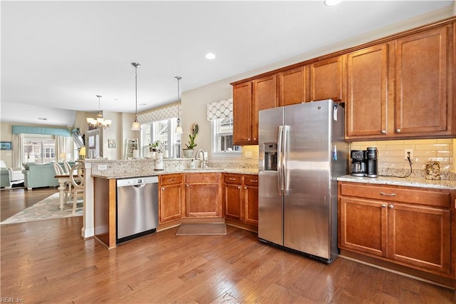 kitchen with appliances with stainless steel finishes, decorative backsplash, hanging light fixtures, kitchen peninsula, and light wood-type flooring