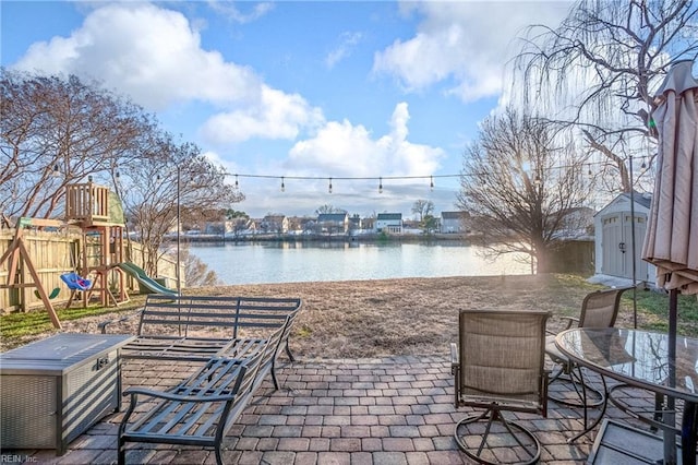 view of patio featuring a playground, a water view, and a shed