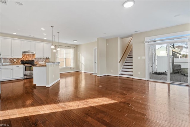 kitchen featuring electric stove, white cabinetry, backsplash, a center island with sink, and decorative light fixtures