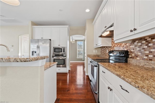 kitchen featuring white cabinets, backsplash, stainless steel appliances, light stone countertops, and dark wood-type flooring