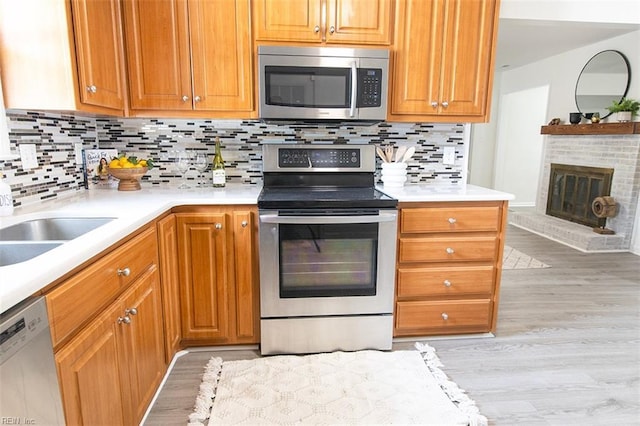 kitchen with sink, light hardwood / wood-style flooring, stainless steel appliances, a brick fireplace, and decorative backsplash