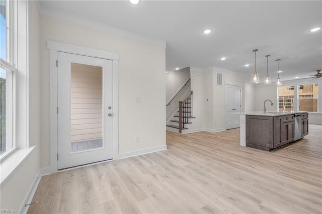 kitchen with pendant lighting, an island with sink, sink, stainless steel dishwasher, and light hardwood / wood-style floors