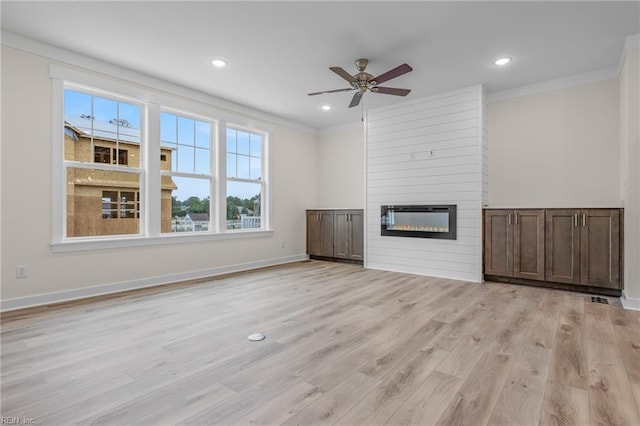 unfurnished living room featuring crown molding, a large fireplace, ceiling fan, and light wood-type flooring