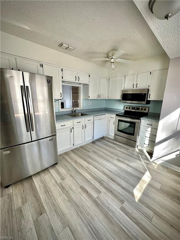 kitchen with sink, white cabinets, ceiling fan, stainless steel appliances, and light hardwood / wood-style flooring