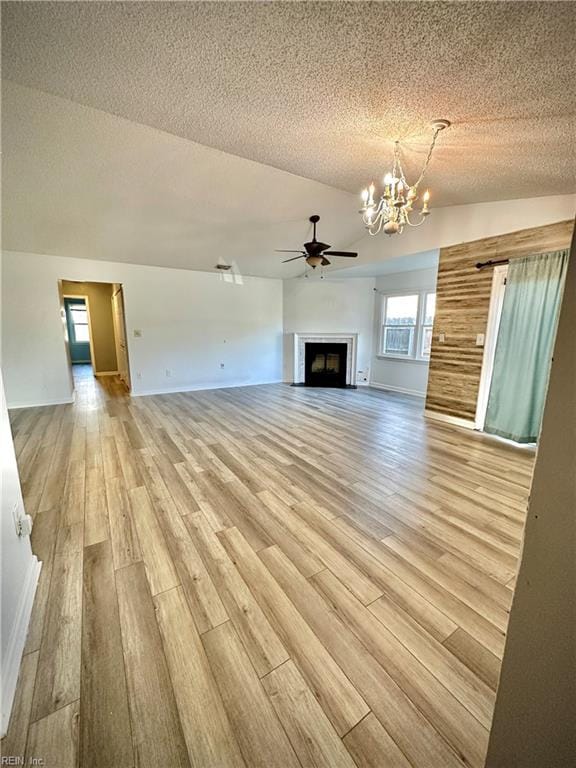 unfurnished living room with ceiling fan with notable chandelier, vaulted ceiling, a textured ceiling, and light wood-type flooring