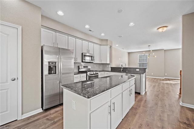 kitchen with dark stone countertops, stainless steel appliances, white cabinets, a kitchen island, and kitchen peninsula