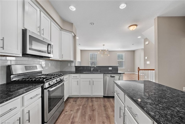 kitchen featuring appliances with stainless steel finishes, decorative light fixtures, sink, white cabinets, and dark stone counters