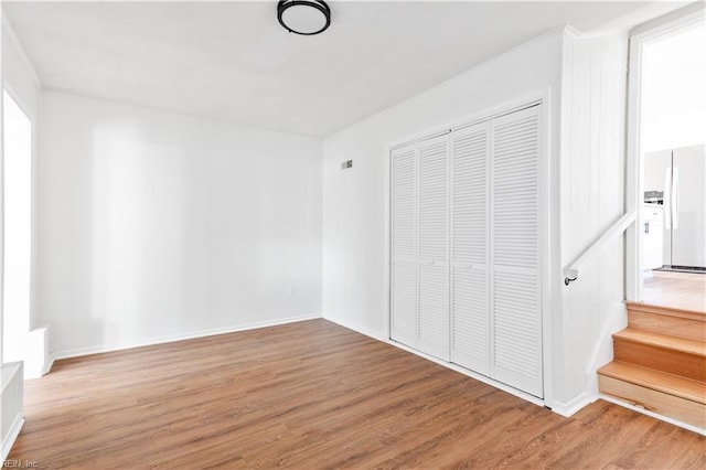 unfurnished bedroom with wood-type flooring, a closet, and white fridge with ice dispenser