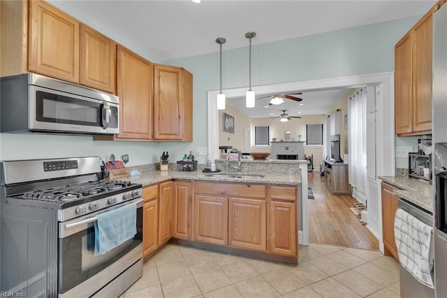 kitchen with pendant lighting, sink, light stone counters, kitchen peninsula, and stainless steel appliances