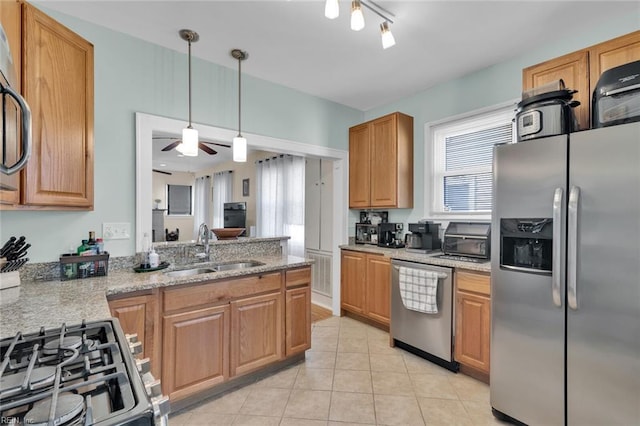 kitchen with sink, hanging light fixtures, light tile patterned floors, appliances with stainless steel finishes, and light stone countertops