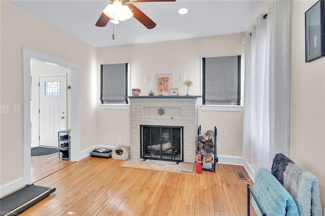 living room with wood-type flooring, ceiling fan, and a fireplace