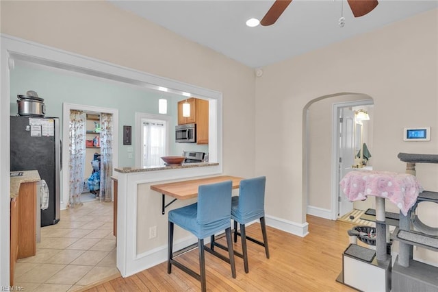 kitchen featuring appliances with stainless steel finishes, a kitchen bar, ceiling fan, light stone counters, and light wood-type flooring