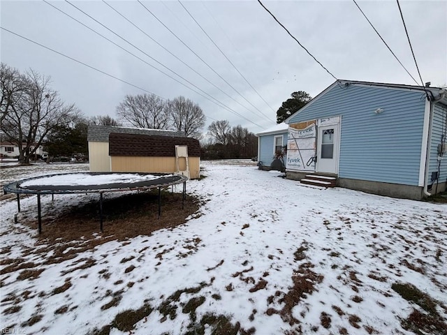 yard covered in snow featuring a trampoline and a storage unit