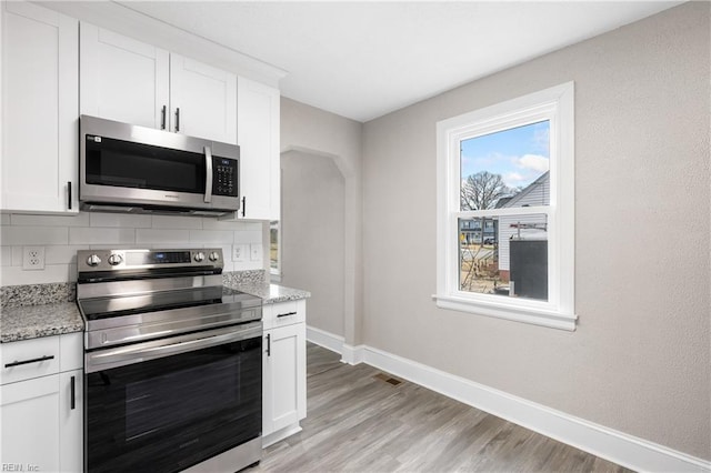 kitchen with white cabinetry, stainless steel appliances, light stone counters, light hardwood / wood-style floors, and decorative backsplash