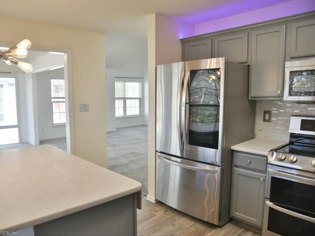 kitchen featuring tasteful backsplash, an inviting chandelier, light hardwood / wood-style flooring, gray cabinets, and stainless steel appliances