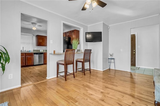 kitchen with a kitchen bar, black fridge, stainless steel dishwasher, ornamental molding, and light hardwood / wood-style floors