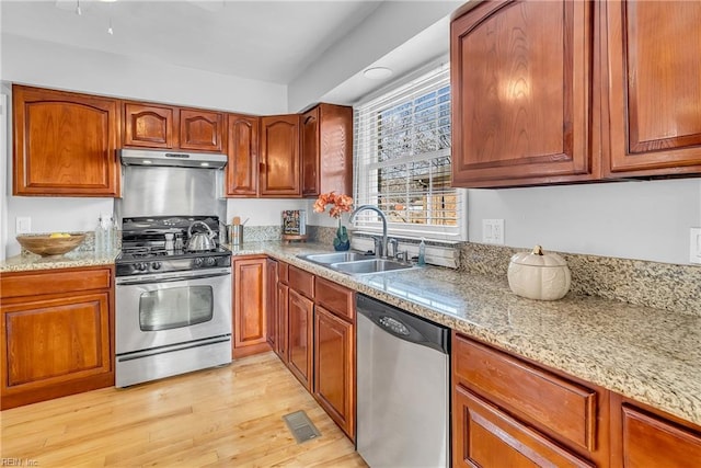 kitchen with light stone countertops, appliances with stainless steel finishes, sink, and light wood-type flooring