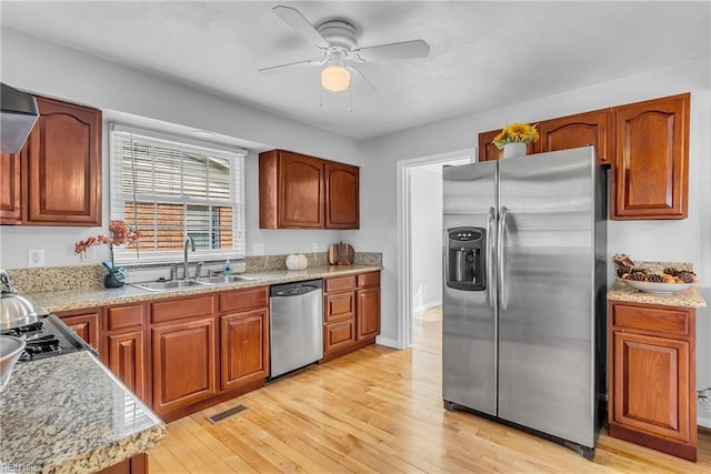 kitchen featuring stainless steel appliances, sink, light stone counters, and light wood-type flooring