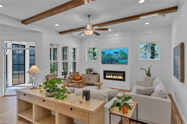 living room featuring beamed ceiling, ceiling fan, a fireplace, and light wood-type flooring