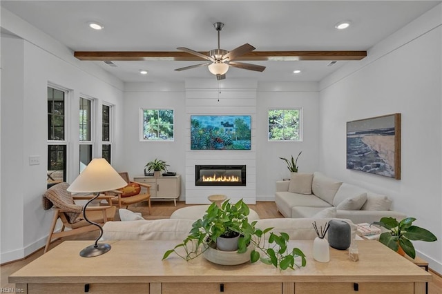 living room featuring ceiling fan, a large fireplace, beam ceiling, and light hardwood / wood-style floors