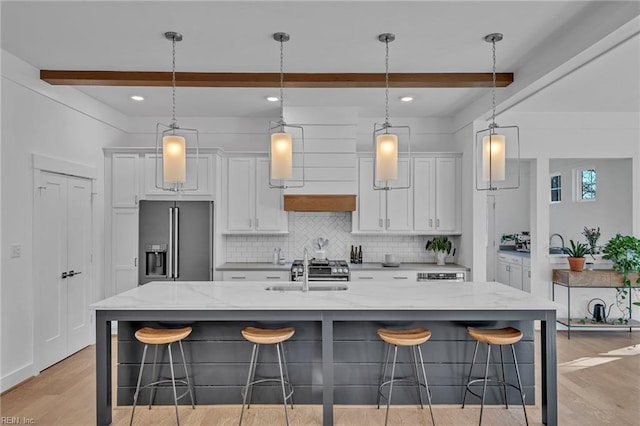 kitchen featuring white cabinets, a kitchen bar, a large island with sink, light stone counters, and high end fridge