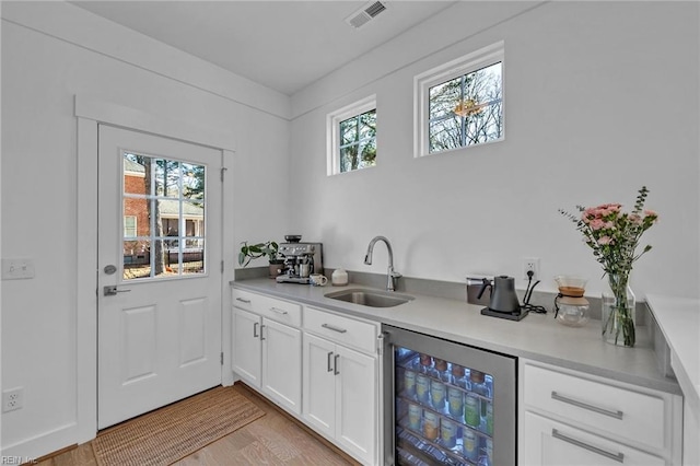 bar with white cabinetry, sink, light hardwood / wood-style flooring, and beverage cooler