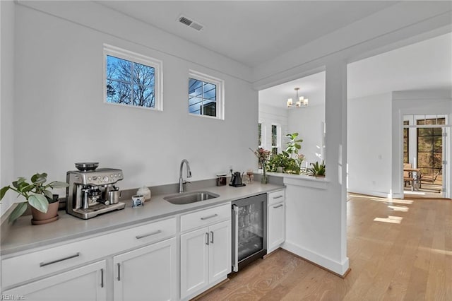 kitchen featuring sink, a healthy amount of sunlight, beverage cooler, light hardwood / wood-style floors, and white cabinets